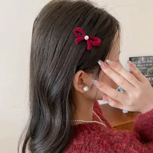 Close-up detail of an elegant red velvet bow hair clip with a pearl center on a model