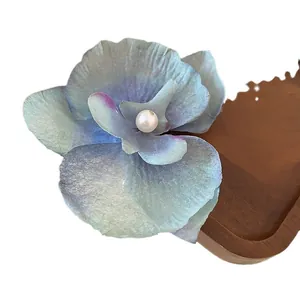Mint blue orchid hair clip with central pearl detail on wooden background