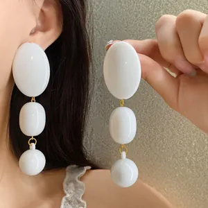 Dettaglio di orecchini a pendente in acrilico bianco con tre perle su modella asiatica