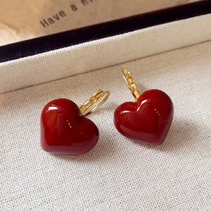 Close-up of elegant red heart enamel earrings with gold hoop on textured fabric