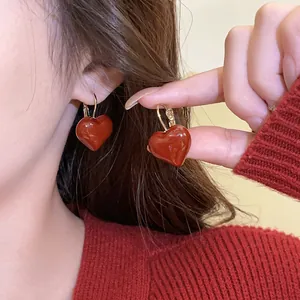 Detailed macro view of glossy red heart drop oil earrings showing the wearing effect