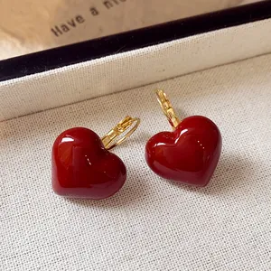 Close-up detail of vintage red oil-dripped heart earrings on beige textured fabric