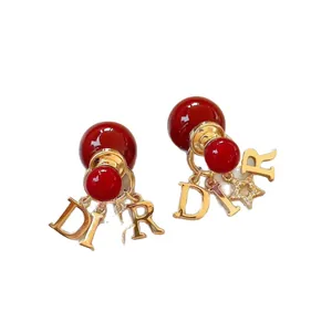 Eleganti orecchini a perno con perle rosse, lettere dorate e ciondolo a stella brillante.