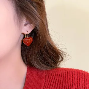 Close-up view of a glossy Ankara red heart-shaped earring worn on a model's ear.