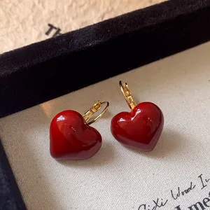 Close-up of elegant red enamel heart hoop earrings on a beige textured background