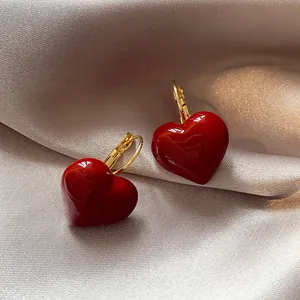 Close-up of red oil-dripped heart earrings with gold lever-back on silk fabric