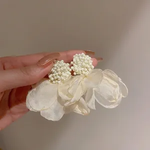 Dettaglio di orecchini eleganti con perle bianche e petali di fiori in rete color crema