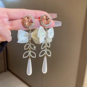 Primo piano di eleganti orecchini lunghi con gemme rosa, fiocchi e perle