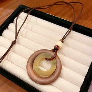 Macro detail of vintage geometric wood and resin pendant on a long brown leather cord.