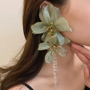 Close-up view of elegant green mesh flower earrings with long crystal tassels on a model's ear