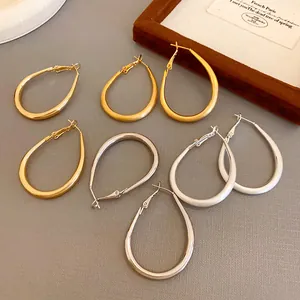 Collection of oval U-shaped hoop earrings in gold and silver finishes on a textured backdrop