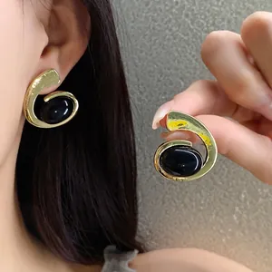 Boucles d'oreilles spirale dorées vintage avec pierres ovales noires sur l'oreille