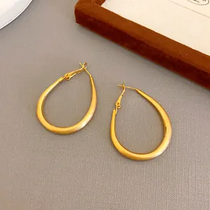 Detailed view of minimalist gold-plated oval U-shaped hoop earrings on grey surface