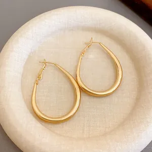 Macro view of minimalist gold-plated U-shaped hoop earrings on a soft textured plate.