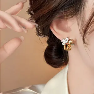 Close-up view of elegant silver stud earrings with square amber crystal and golden pearl