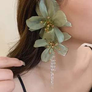 Detail of long green mesh flower earrings with crystal tassels on a model.