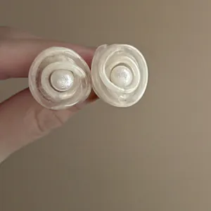Dettaglio ravvicinato di eleganti orecchini a fiore in rete crema con perla centrale