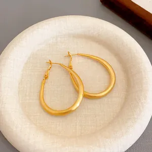 Elegant close-up view of gold-plated U-shaped oval hoop earrings on a textured tray
