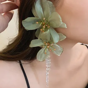 Close-up detail of oversized green mesh flower earring with crystal tassel on model