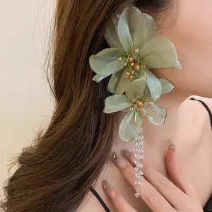 Close-up of elegant green mesh flower earrings with crystal tassels on model's ear