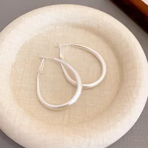 Minimalist silver U-shaped hoop earrings with a matte finish on a textured beige display plate