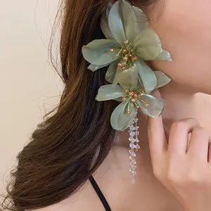 Close-up of elegant green mesh flower earrings with crystal tassels on a model