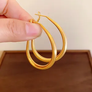 Close-up view of gold-plated minimalist U-shaped oval hoop earrings held by hand