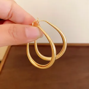 Close-up view of gold-plated U-shaped oval hoop earrings held by hand.