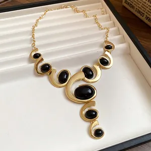 Détail d'un collier vintage doré avec des pierres ovales noires et des motifs en spirale.