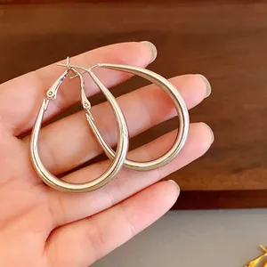 Minimalist silver-colored oval U-shaped hoop earrings held in hand