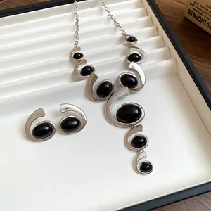 Gros plan d'une parure de bijoux vintage avec spirales géométriques et pierres noires.