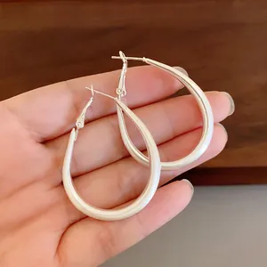Close-up of large minimalist oval U-shape silver hoop earrings held in hand for size reference