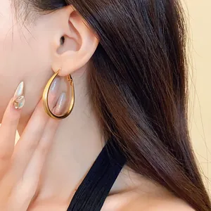 Detailed close-up of minimalist gold-plated oval hoop earrings worn by a model