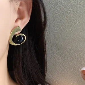 Détail de la boucle d'oreille rétro en spirale dorée avec une pierre noire ovale