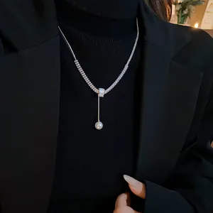 Detailed view of an elegant zircon necklace with a dangling white pearl on a black blazer.