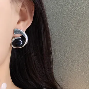 Détail en gros plan d'une boucle d'oreille spirale argentée avec une gemme noire ovale