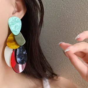 Close-up of oversized acrylic marbled earrings in a colorful tiered teardrop design