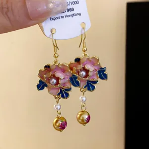 Close-up of elegant enamel flower earrings with faux pearls and dangling golden beads.