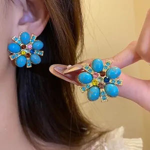 Dettaglio macro di orecchini vintage a fiore con pietre turchesi e cristalli colorati