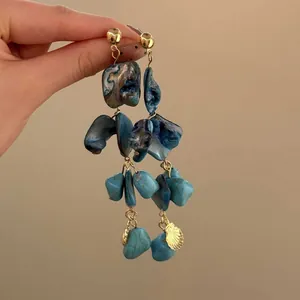 Dettaglio di orecchini bohémien con nappe, pietre blu irregolari e ciondoli a conchiglia d'oro.