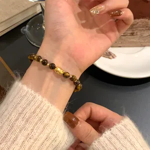 Close-up view of tiger eye stone beads and gold-plated fish charm on jewelry bracelet