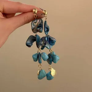 Dettaglio di orecchini a nappa in conchiglia blu irregolare in stile boho con ciondolo oro