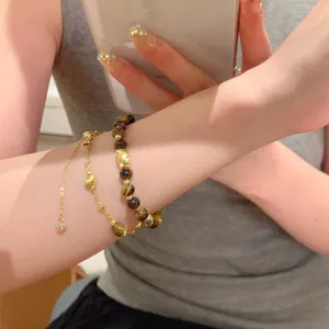 Close-up of tiger eye bead bracelet and gold chain on woman's wrist detail view