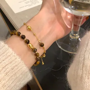 Close-up of a gold-plated tiger eye stone bracelet on a wrist holding a wine glass