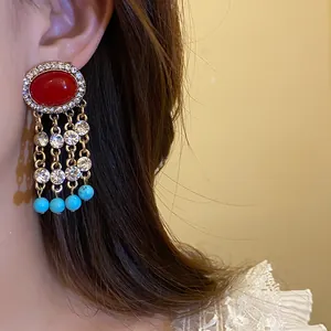Dettaglio di orecchini vintage con pietre rosse, nappe e perle di colore azzurro