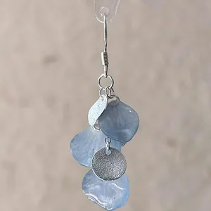 Detail view of a handmade earring featuring gradient blue petals and a silver disk