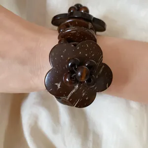 Primo piano di un braccialetto etnico in legno e fiori di cocco su un polso reale.