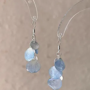 Detail showing gradient blue shell petal earrings with textured silver circular discs