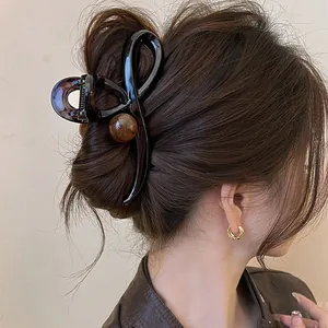 Vue détaillée d'une pince à cheveux croisée marron foncé avec une boule décorative