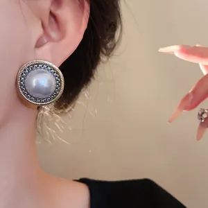 Dettaglio ravvicinato di un orecchino vintage con perla finta e bordo intrecciato